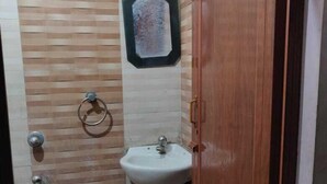 A small bathroom with a wooden door, a white sink, a shower, and a tiled wall. - Deteex Classic Inn (Barakpur)