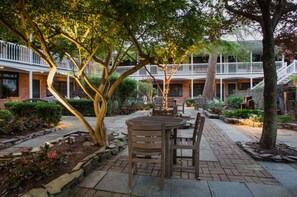 A courtyard with a wooden table and chairs, surrounded by brick pathways and greenery. - Palmer House King | Vaulted Ceilings & Deck (Rehoboth Beach)
