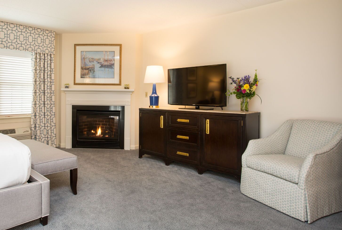 A hotel room with a fireplace, a television, a sofa, and a decorative vase.