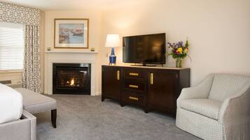 A hotel room with a fireplace, a television, a sofa, and a decorative vase.
