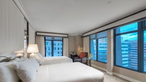 Camera d'albergo con due letti, ampie finestre, un comodino, una lampada e vista sulla città.