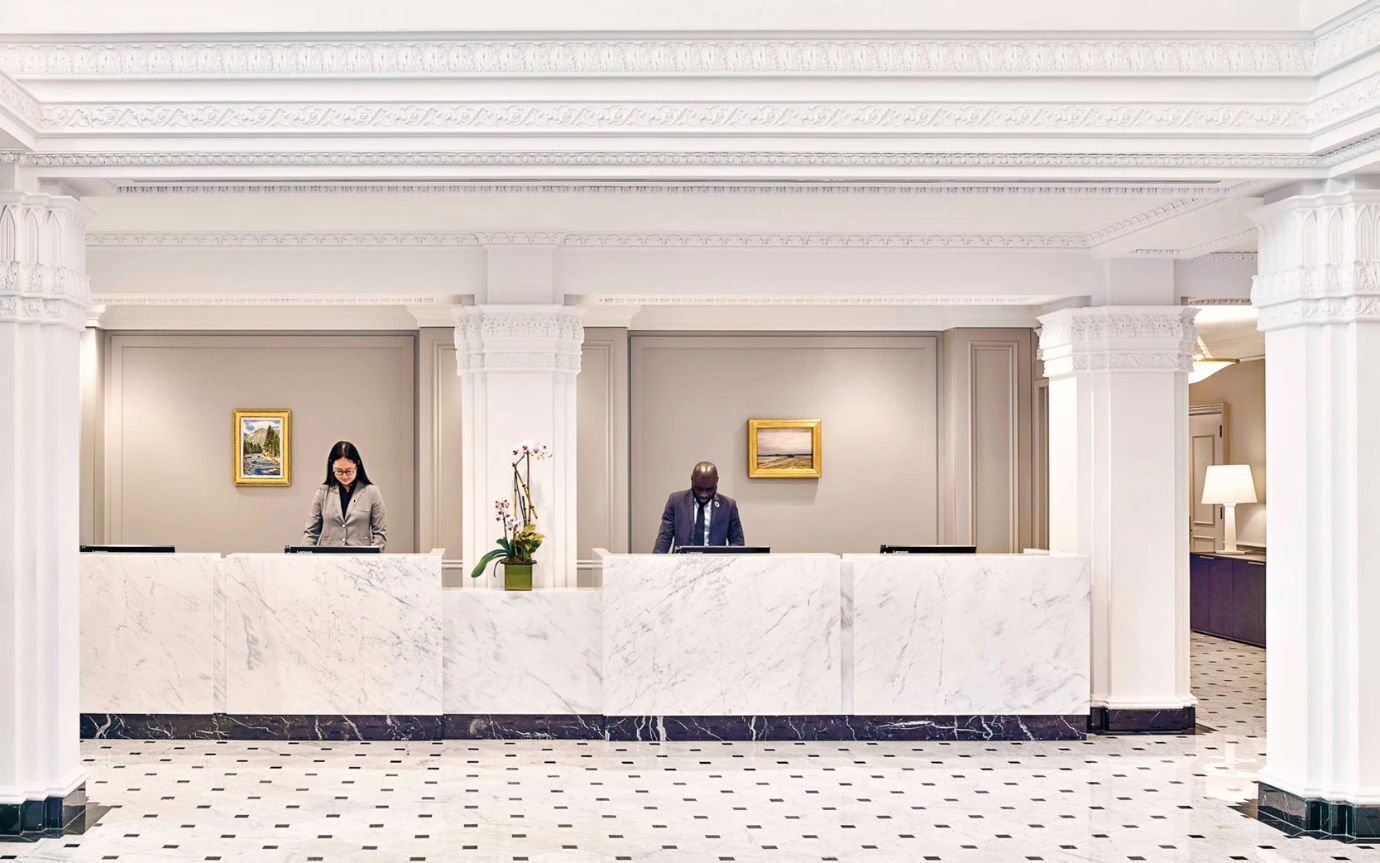 Un'area reception di un hotel con banconi in marmo, opere d'arte incorniciate alle pareti e un pavimento decorato.