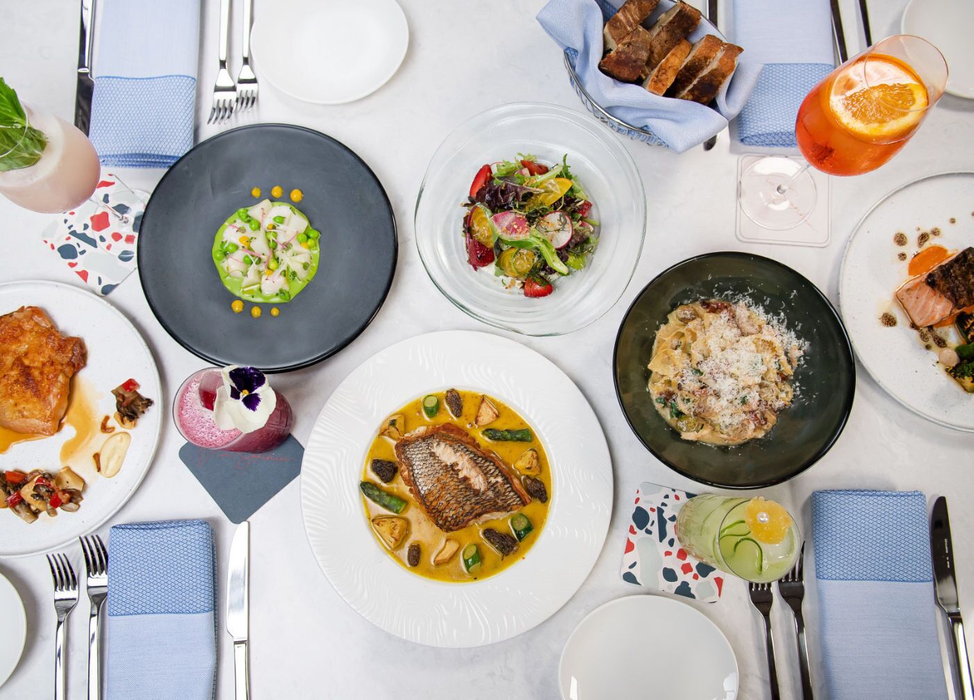 A table set with various dishes, including fish, pasta, and salads, suggesting a meal setting.