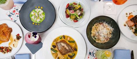 Une table dressée avec différents plats, notamment du poisson, des pâtes et des salades, ce qui laisse supposer qu’il s’agit d’un repas.