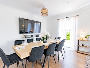 A modern dining area with a wooden table set for six, black chairs, a chandelier, a large mirror, and a view of greenery outside. - Hawkwell Retreat 5 Bedroom home | Hockley - Pass the Keys (Hawkwell)
