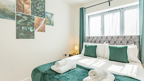 Habitació d'hotel amb llit, roba de llit verda, finestra amb cortines i decoració mural.