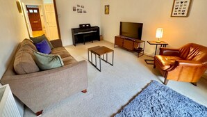 Een woonkamer met een bank, een salontafel, een televisie, een leren fauteuil en een bijzettafeltje met een lamp.