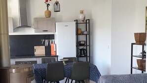 Una sala de estar moderna con un sofá, una mesa de centro y un comedor con sillas y una mesa. Hay una cocina con estufa, fregadero y armarios.