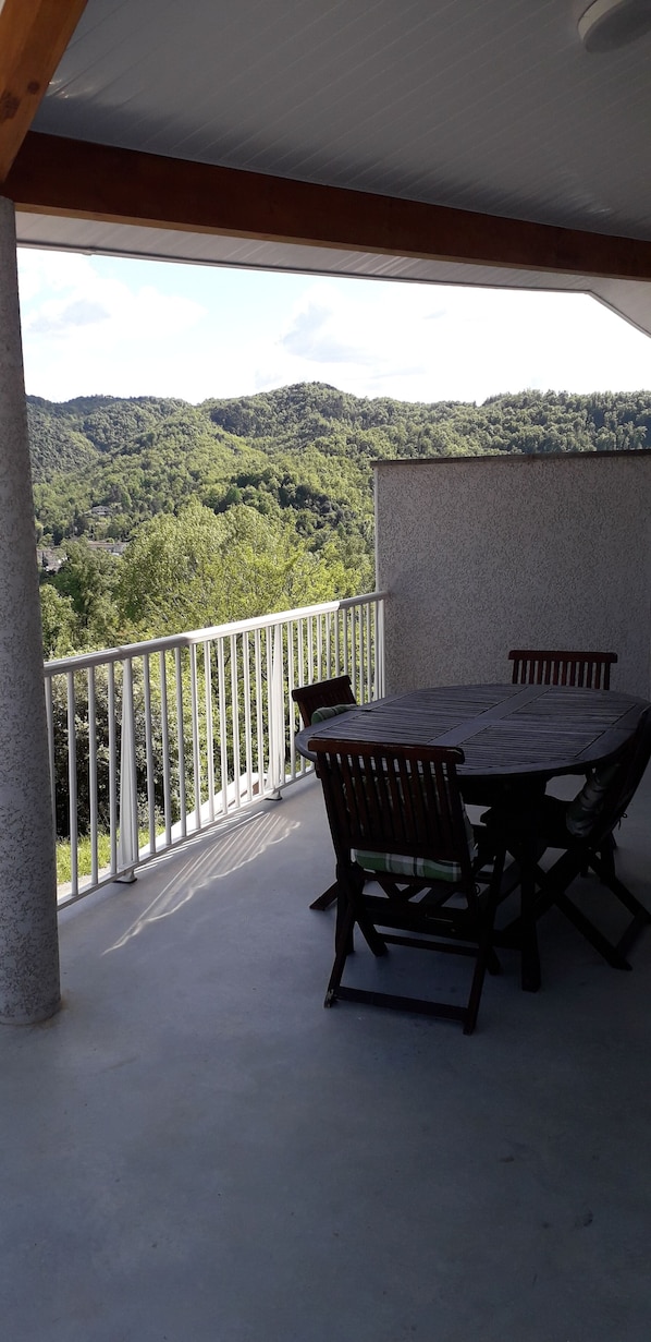 A balcony with a table and chairs, overlooking a mountainous landscape.