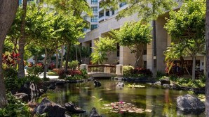 Un jardin intérieur paisible, avec un bassin, entouré d’une végétation luxuriante et agrémenté d’un pont.