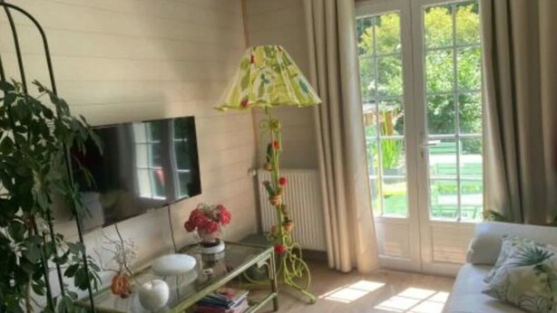 Olohuone, jossa on seinälle asennettu televisio, vihreä pöytä koriste-esineineen, sohva ja ikkuna, jossa on verhot.