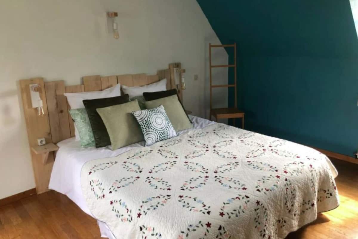 Een slaapkamer met een houten hoofdbord, een witte sprei en een houten ladder tegen een blauwgroene muur.