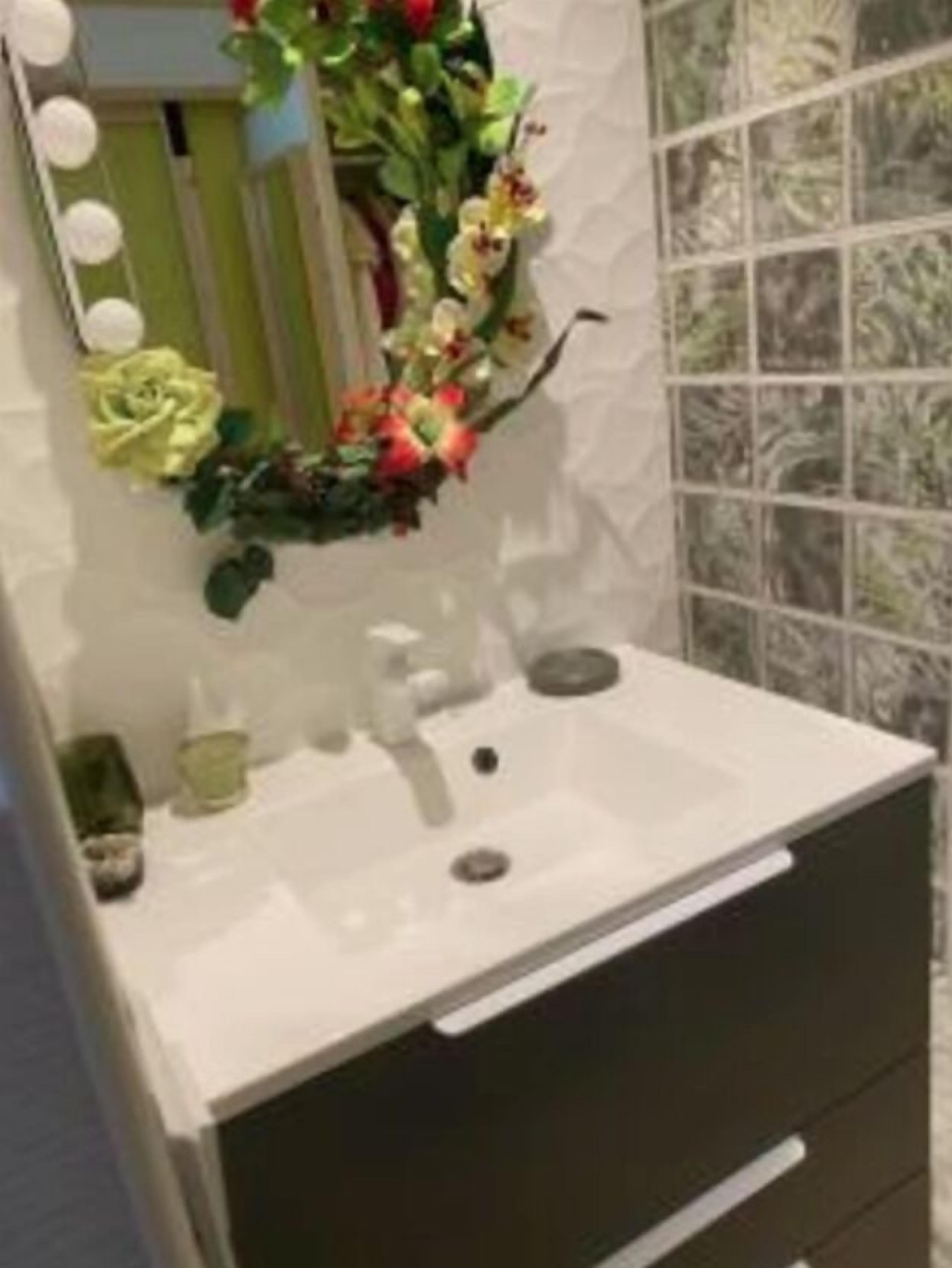 Ein Badezimmer mit einem weißen Waschbecken, grünen und gelben Blumen und einem Spiegel mit Beleuchtung.