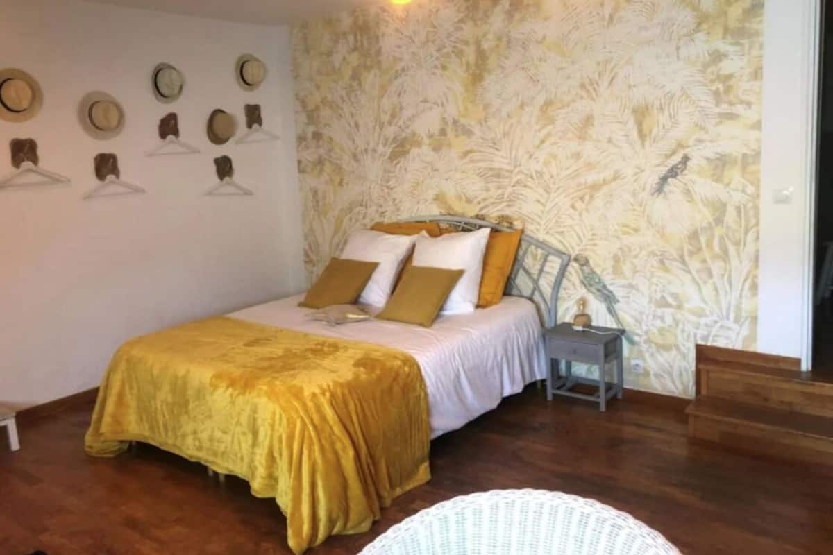 Een slaapkamer met een bed, nachtkastje en kapstokhaakjes aan de muur.