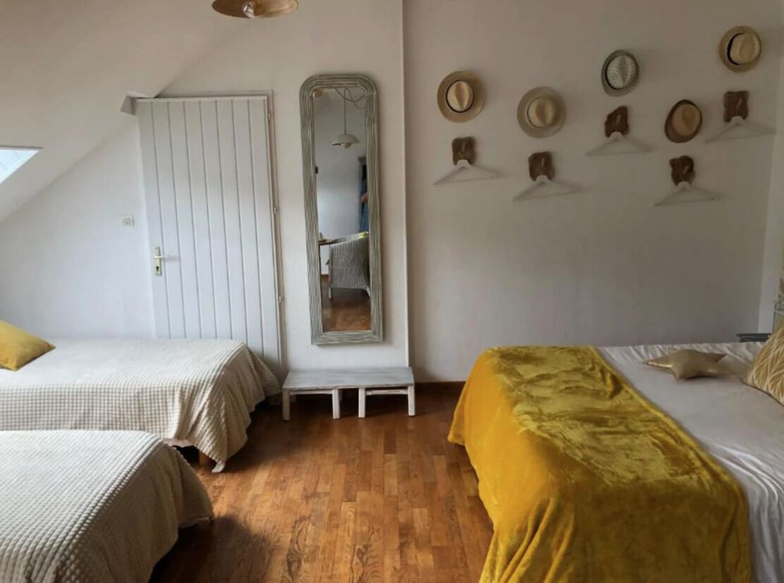 Une chambre avec deux lits, un grand miroir et un mur où sont accrochés des chapeaux.