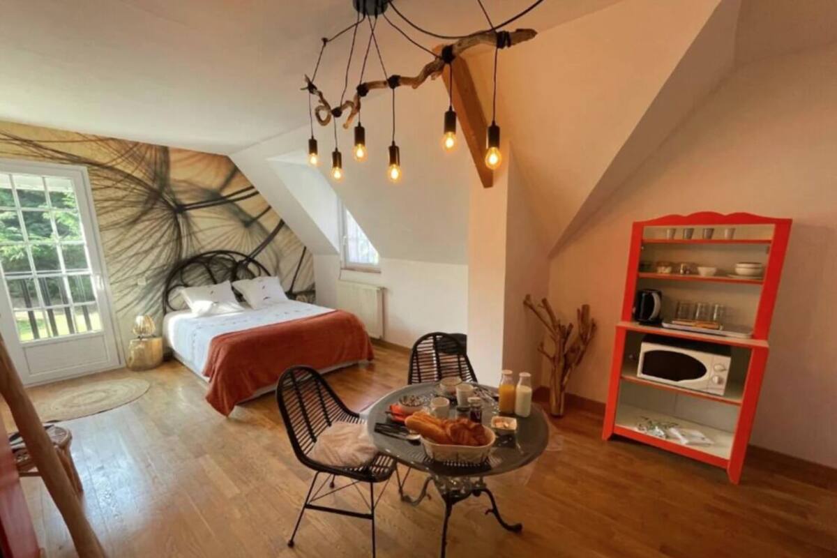 Een knus ingerichte kamer met een bed, een eettafel met ontbijt, een rode boekenkast en een bijzondere plafondlamp.