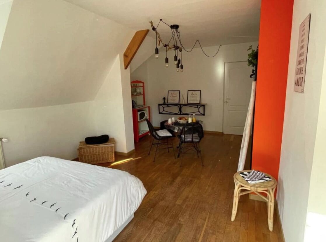 Ein Schlafzimmer mit einem Bett, einem Schreibtisch und einem Stuhl. Der Boden ist aus Holz und die Wand ist weiß.