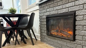 Une cuisine moderne avec une cheminée en pierre, une table à manger avec des chaises et une vue sur la ville par la fenêtre.