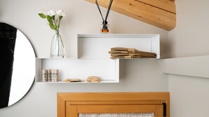 A modern room with a wooden ceiling, white walls, and a round mirror. There are white shelves with various items, including a vase with flowers, candles, and folded towels. - BORGO PAOLIN - Rooms in the Vineyard. A journey between culture and relaxation in the countryside. (Veneto)