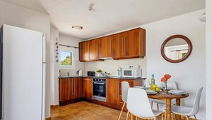 A compact kitchen with wooden cabinets, a built-in oven, and a dining area with a round table and chairs.