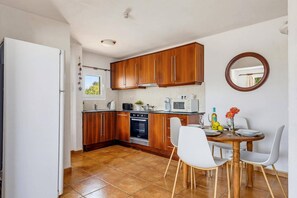 A compact kitchen with wooden cabinets, a built-in oven, and a dining area with a round table and chairs.
