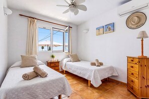 A hotel room with two beds, a ceiling fan, a wooden dresser, and a window with curtains. - Villa Bourgon by Villa Plus (Cala en Porter)