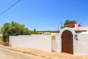 A white-walled building with a wooden door, a mailbox, and a sign indicating a location. - Villa Bourgon by Villa Plus (Cala en Porter)