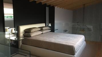 A modern bedroom with a glass bedside table, a bed with a beige headboard, and a dark wall.