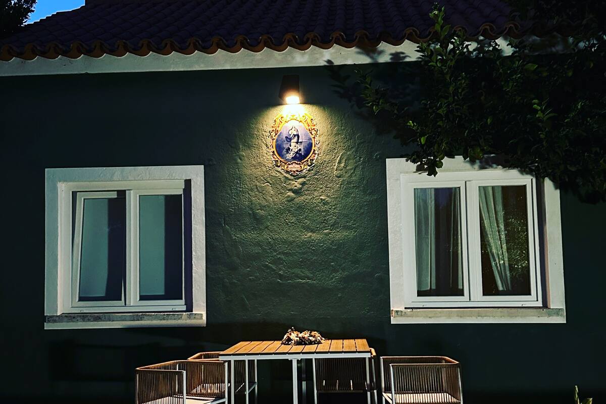 A building with two windows, a table with chairs, and a decorative light fixture on the wall.