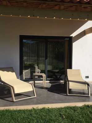 A modern outdoor seating area with two lounge chairs and a small table, a sliding glass door leading to a patio, and a well-maintained lawn. - Horta dos Cedros  (Tomar)