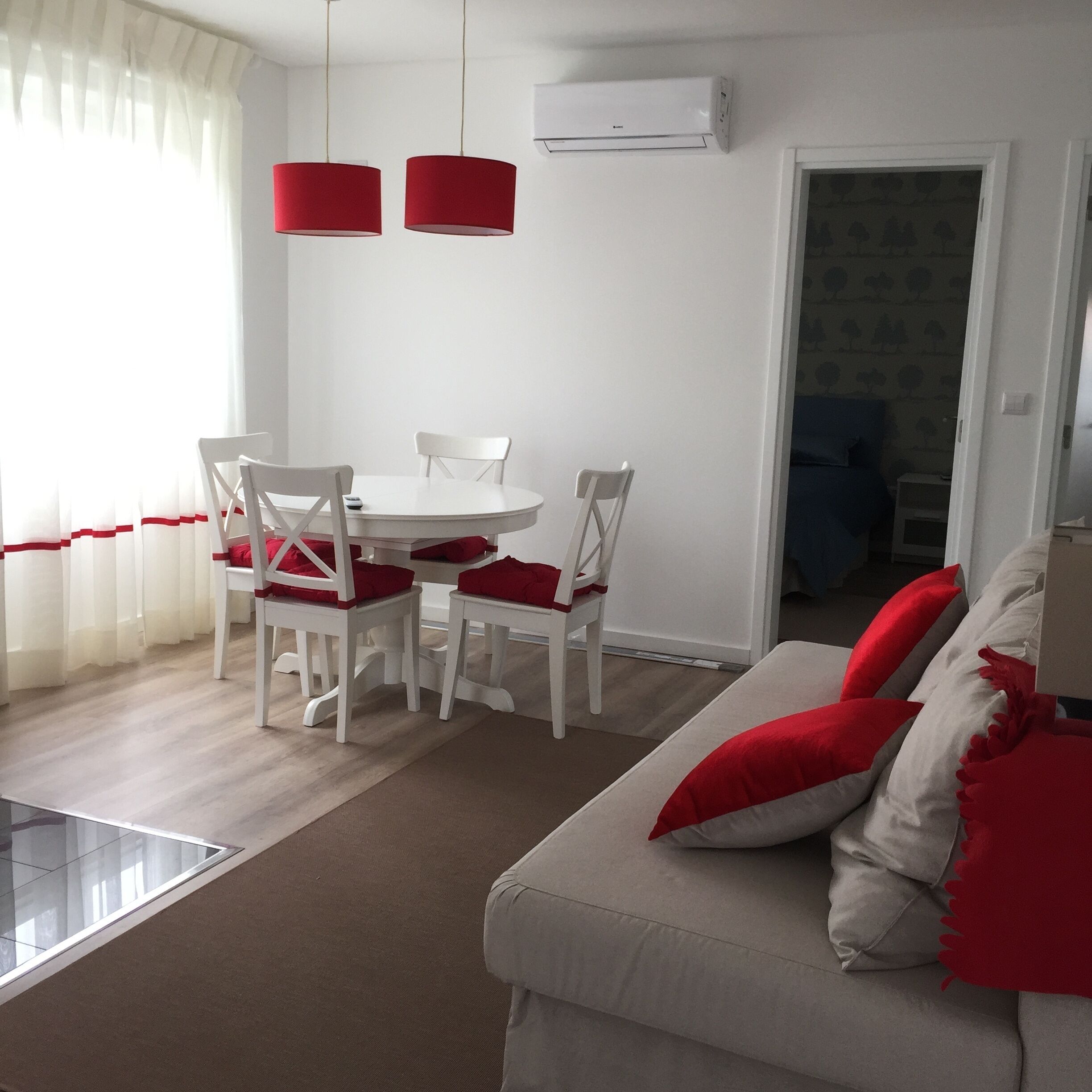 A dining area with a white table and chairs, red cushions, and a red pendant light.