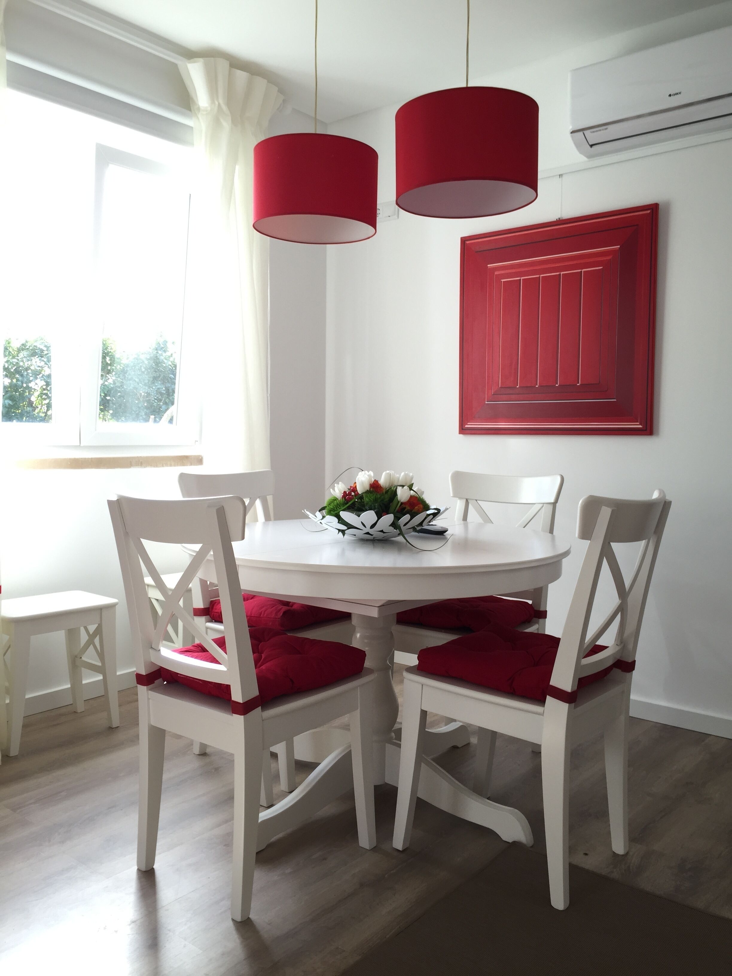 A dining area with a white table and chairs, red cushions, and a vase of flowers.