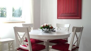 A dining area with a white table and chairs, red cushions, and a vase of flowers.