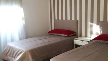 A hotel room with two beds, a striped wall, and a window with curtains.