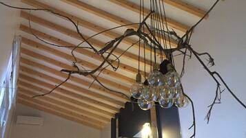 A room with a sloped ceiling, exposed wooden beams, a bed with a headboard, and a hanging light fixture with clear glass bulbs.