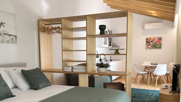 A bedroom with a large bed, a wooden desk, a chair, and a small dining area. - Horta dos Cedros  (Tomar)