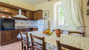 Cucina con pensili in legno, zoccolo piastrellato, piano cottura e tavolo da pranzo con sedie.