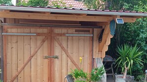 A wooden garage with a metal door, a bicycle, and various potted plants.