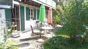 A patio area with a table and chairs, a hanging bird feeder, and a garden with various plants and flowers.