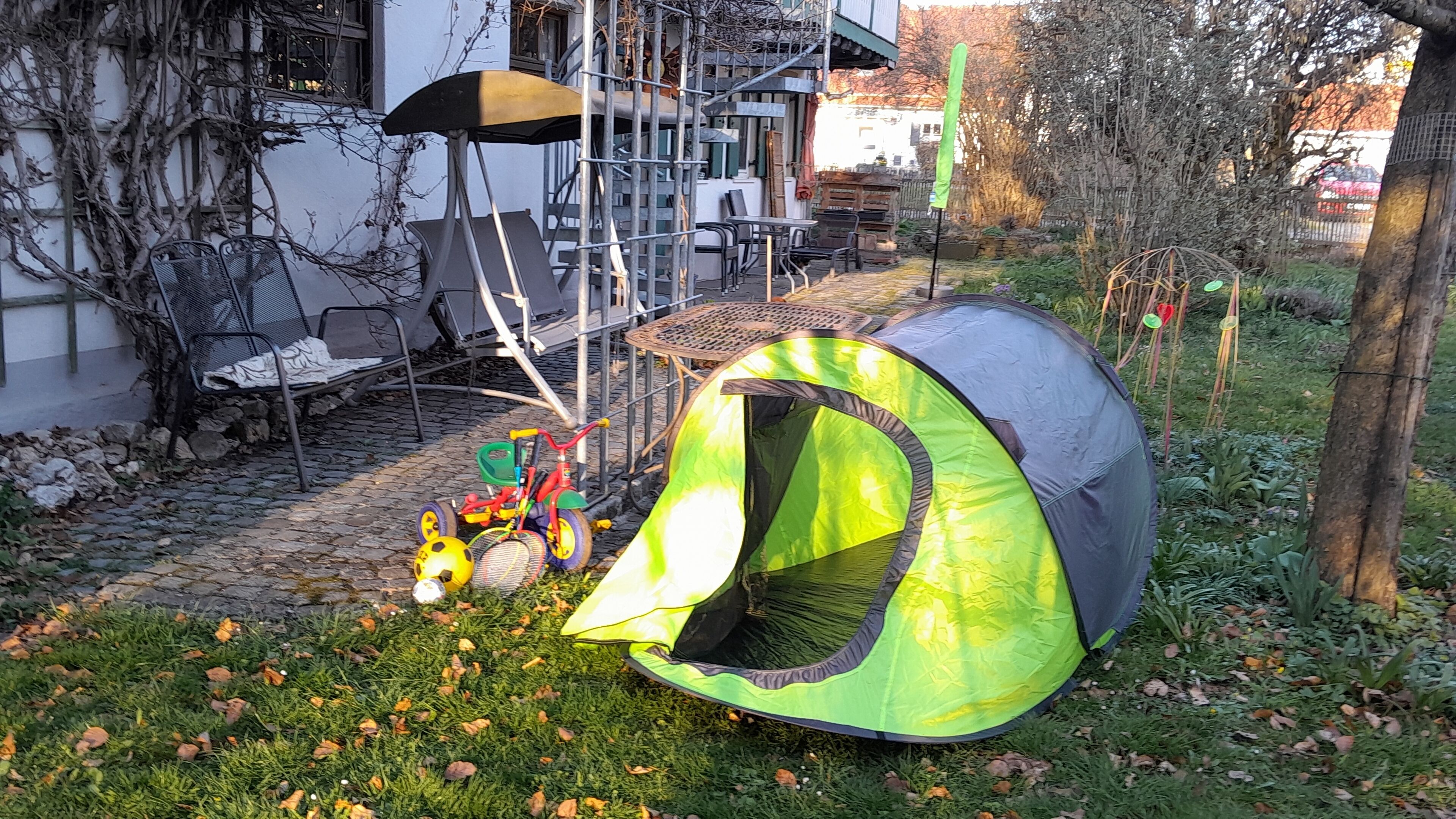 Una tenda verde e grigia montata in un giardino, con una bicicletta e un casco nelle vicinanze.
