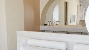 Een moderne slaapkamer met een groot bed, een houten hoofdbord, een ronde spiegel en een ingebouwde wastafel.
