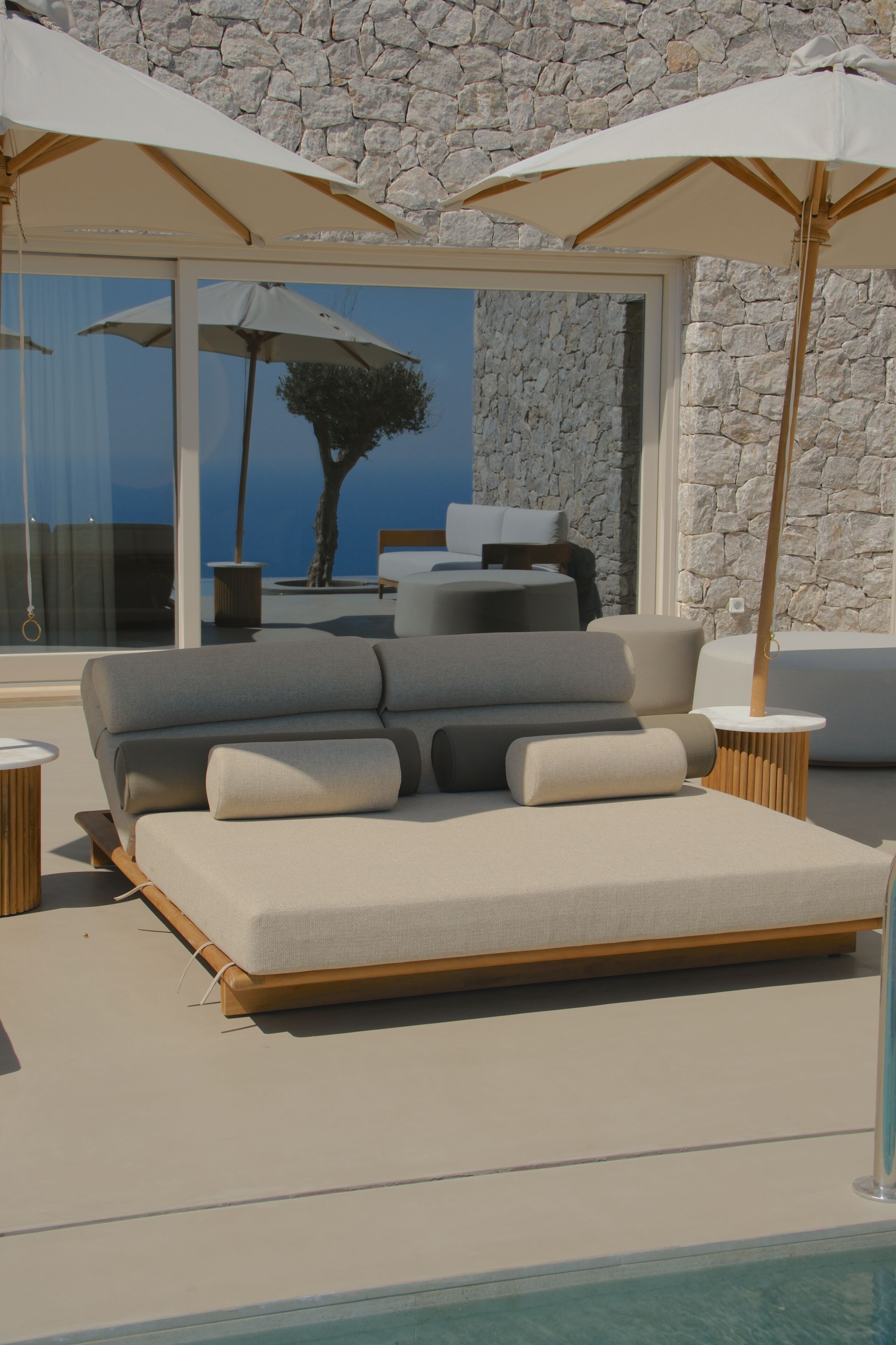 A modern outdoor lounge area with a sofa, two umbrellas, and a pool.