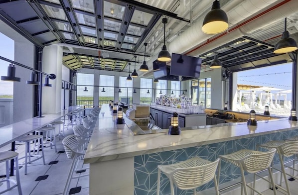 Un espace bar moderne avec de hauts plafonds, de grandes fenêtres et un long comptoir agrémenté de tabourets.