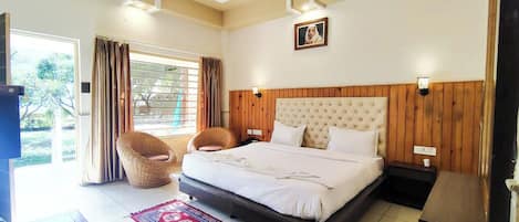 A bedroom with a large bed, a ceiling fan, a window with curtains, a wicker chair, and a red patterned rug.