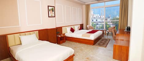 A hotel room with two beds, a desk, a chair, and a large window offering a city view.