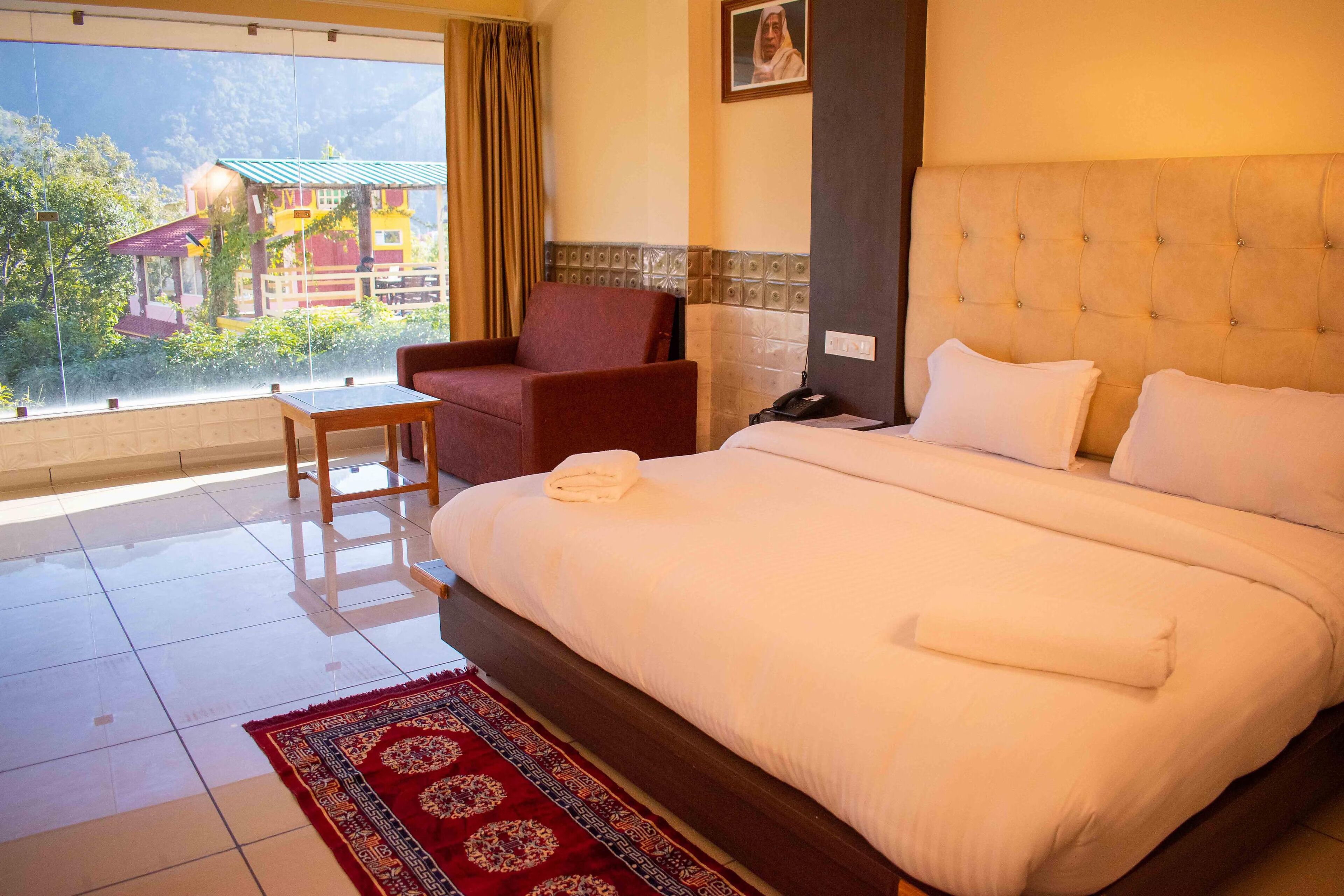A hotel room with a large bed, a chair, a small table, and a view of a building outside.