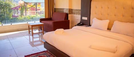 A hotel room with a large bed, a chair, a small table, and a view of a building outside.