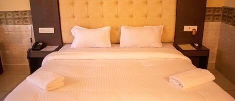 A large bed with white linens and two pillows, a bedside table with a phone and a notepad, and a wall with a decorative panel.