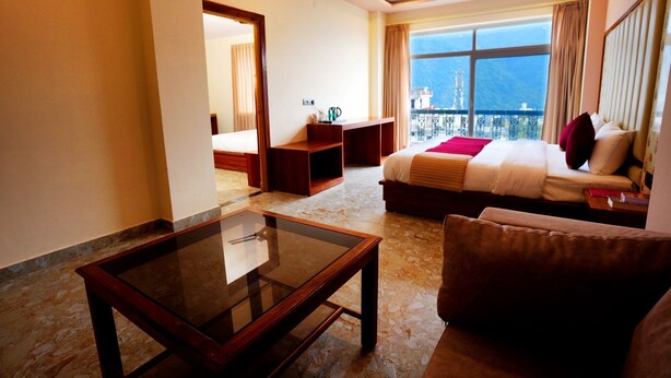 A hotel room with a bed, a glass coffee table, a sofa, a desk, and a balcony with a view. - MVT Resort & Restaurant (Rishikesh)