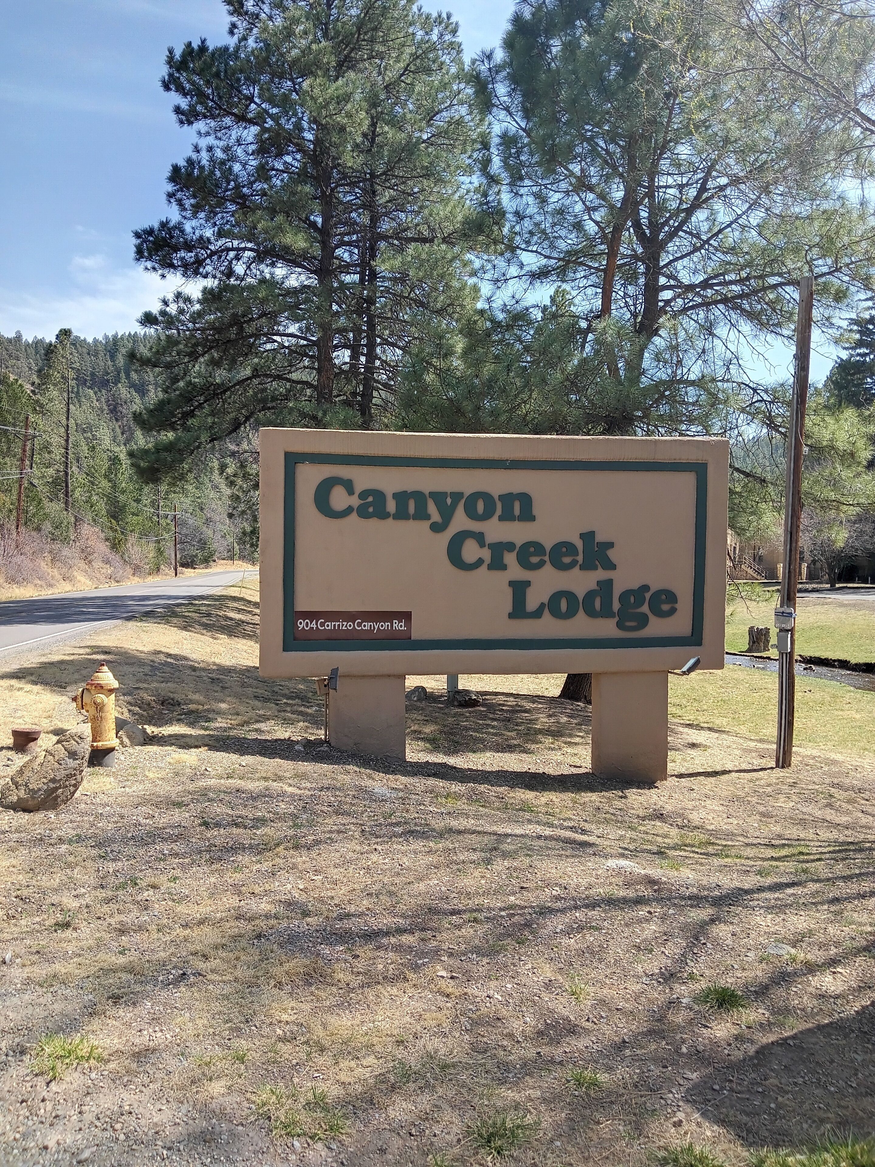 Schild für Canyon Creek Lodge mit freier Sicht auf die Umgebung, darunter ein Hydrant und Bäume.